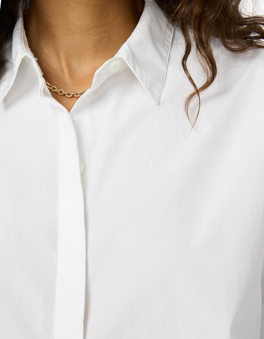 Close-up of a person wearing a white button down shirt with a gold necklace.