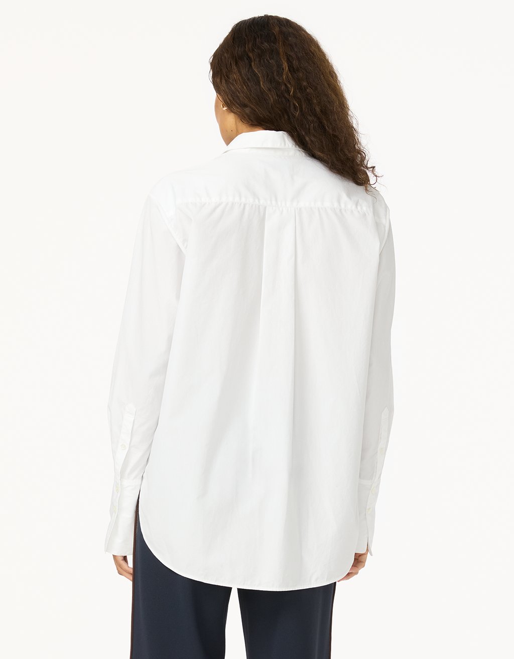 Back view of a woman wearing a white blouse with long sleeves and navy pants on a white background