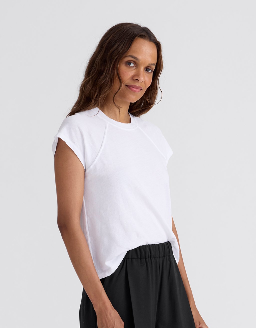Profile of a woman wearing a white raglan t-shirt and gray pants on a white background