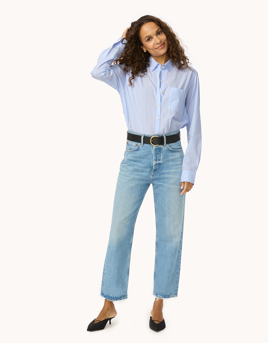 Woman wearing a light blue button down shirt and jeans on a white background