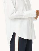 Side view of a person wearing a white blouse with long sleeves and a high-low hemline with navy pants