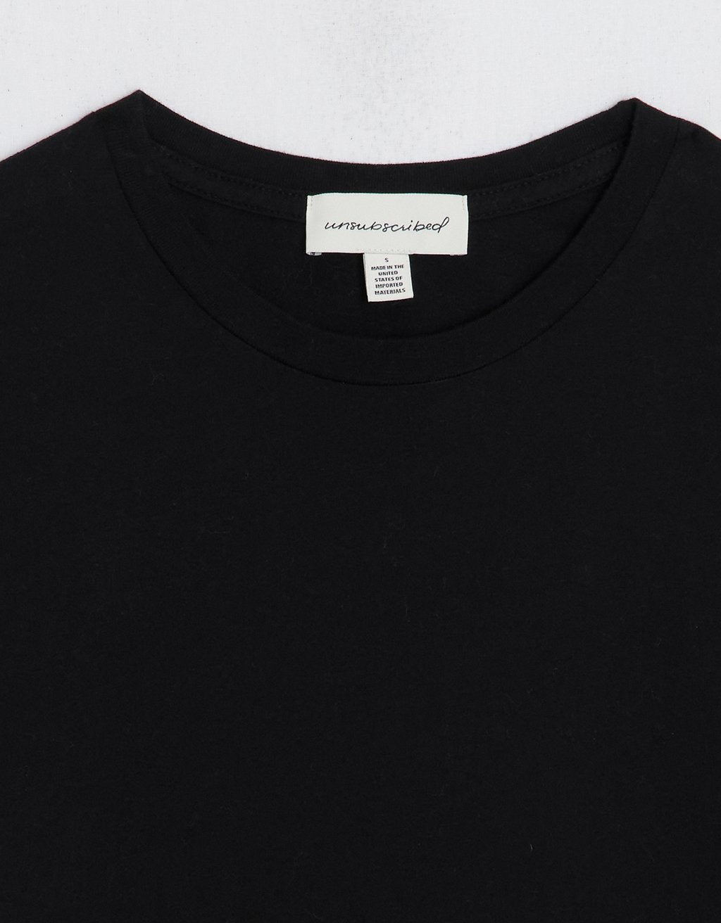 Close-up of a black t-shirt with an unsubscribed brand label on a light gray background