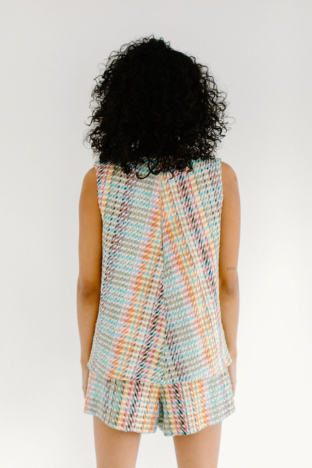 View from behind of a woman with short, black curly hair wearing a tank top and shorts set in a colorful plaid pattern.