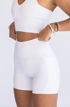 Close up view of a woman's midsection as she adjusts the waistband of her white biker shorts.