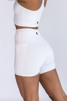 Close up side view of a woman with dark skin wearing a white sports bra and biker shorts set.