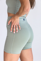 Side view of a woman wearing a sage green workout set with her left hand on her left hip. 