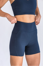 Close up on the torso of a woman wearing a navy sports bra and biker shorts set, pulling up the shorts around her waist.