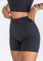 A close up of a woman's midsection as she adjusts the waistband of her black biker shorts. She's wearing a matching top and many stacked bracelets and rings.