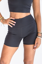 A closeup shot of a woman in a black workout set with her hand on her hip. She is wearing many stacked bracelets on each wrist and has her hip popped and one hand on her hip.